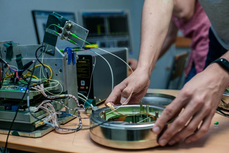 Hands assembling complex electronic components and fiber optic cables in a technical laboratory setting.