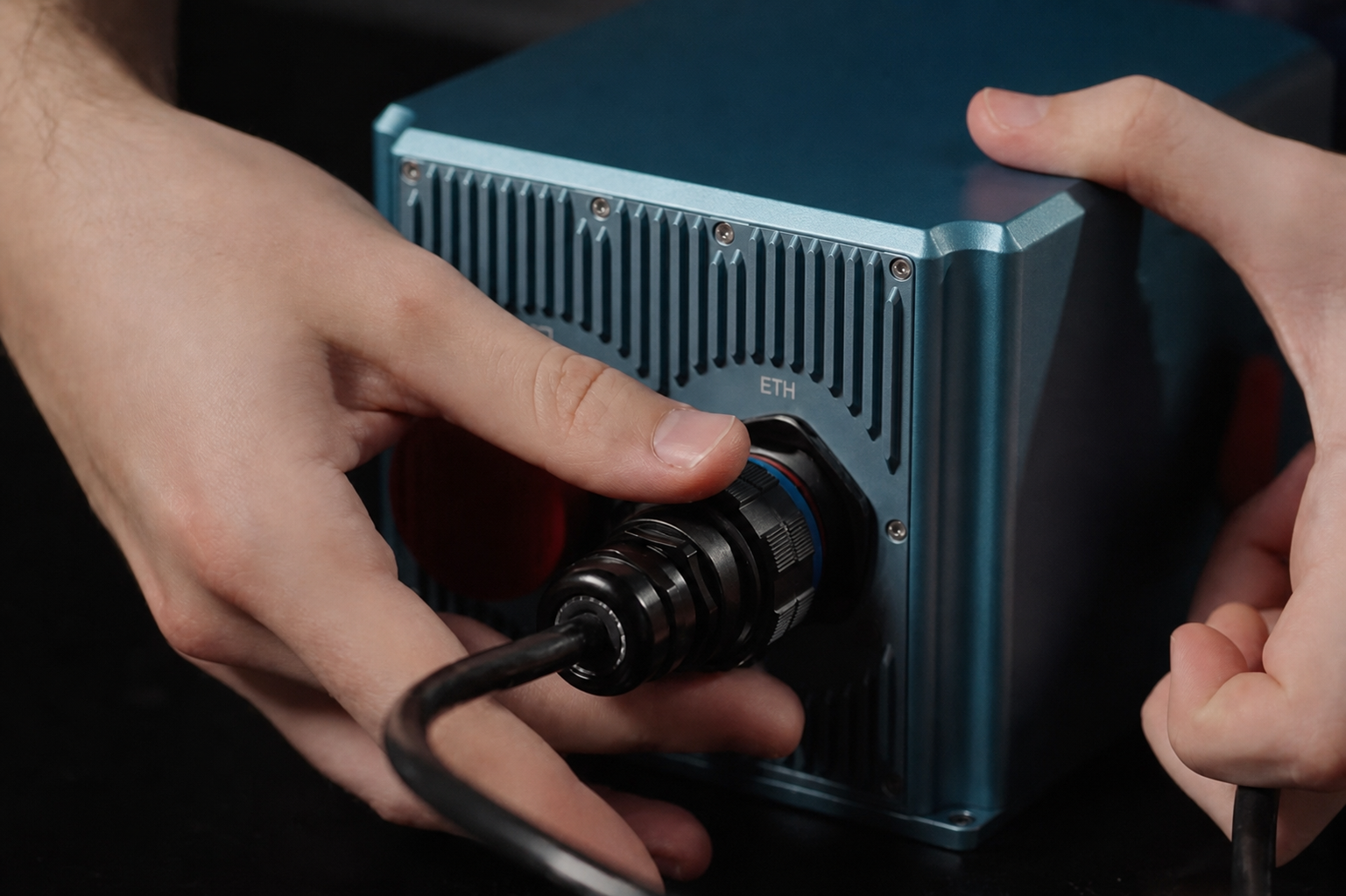 Hands connecting a black cable to the Ethernet port of a blue industrial device.